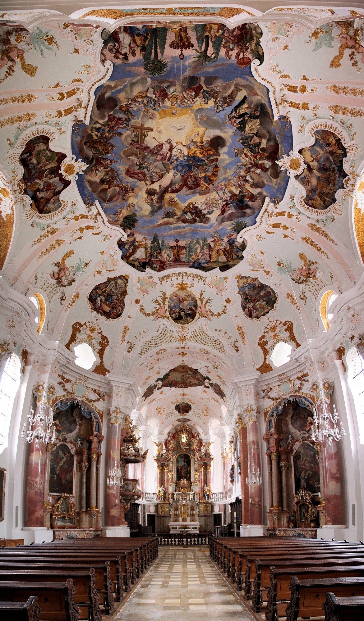 The interior of a Baroque church with white interior and painted scening depicting a religious scene with trompe l'oeil effect