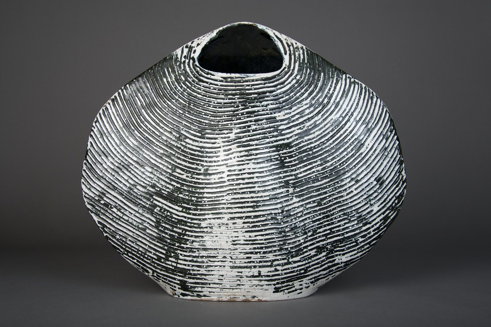 Large cockle shell shape vase with small opening at the top modelled in creamy grey. The ridges in the clap look black.